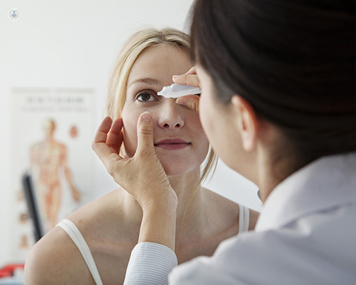 Primer plano de una doctora de espaldas poniendo gotas en los ojos a una paciente que esta de cara a la foto - cirugía del glaucoma - by Top Doctors