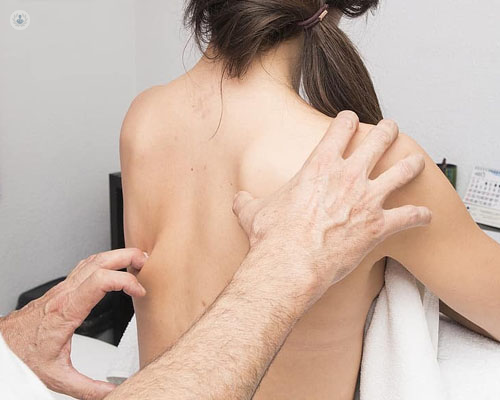 Primer plano de una chica de espaldas y manos del doctor tocándole la espalda - Infiltraciones espalda - by Top Doctors
