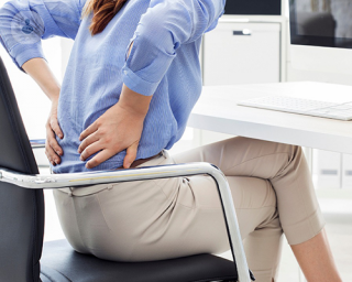 Una mujer en una oficina sujetándose la parte baja de la espalda, a causa del dolor ciático.